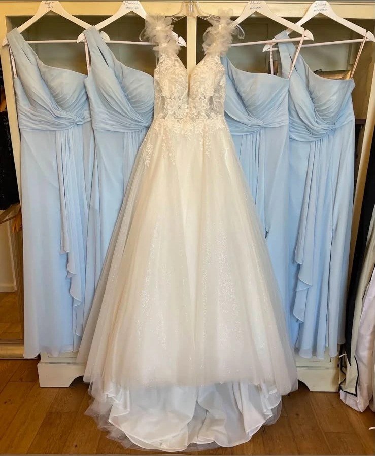 An ivory lace wedding gown flanked by pale blue bridesmaid dresses on the rail at the studio