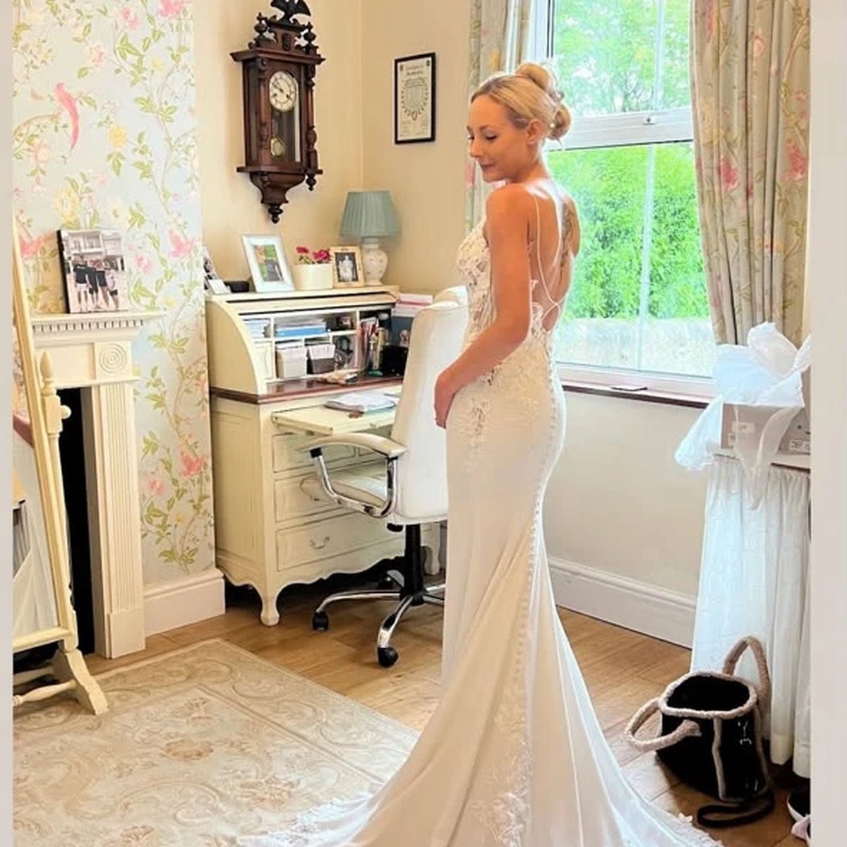 A bride wearing a fitted ivory lace wedding gown with a long train in the studio