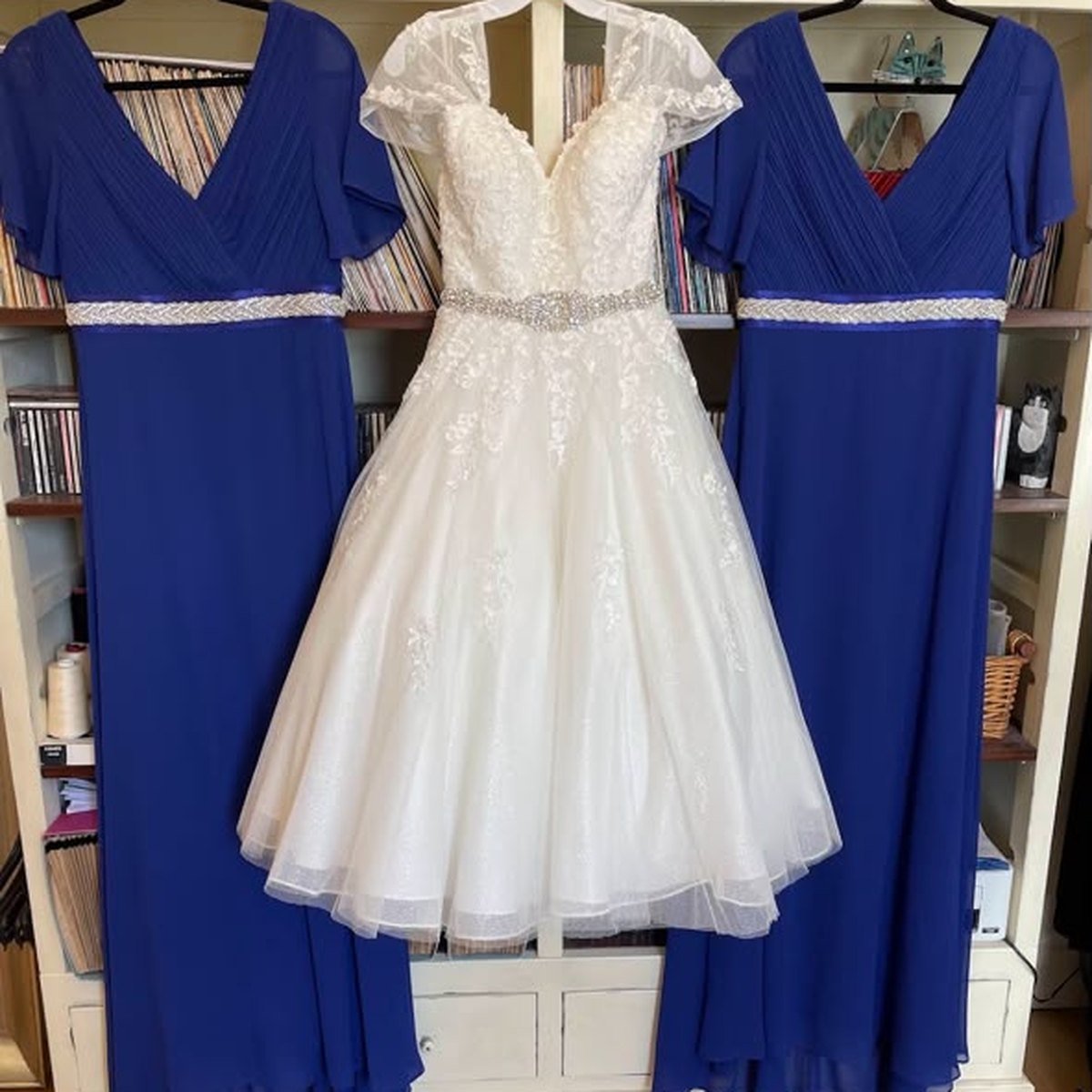 A tea-length ivory lace wedding dress between royal blue bridesmaid dresses